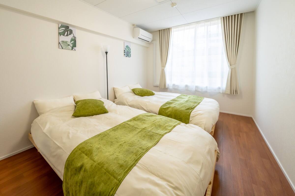 A hotel room with two beds, a standing lamp, and a window with curtains.