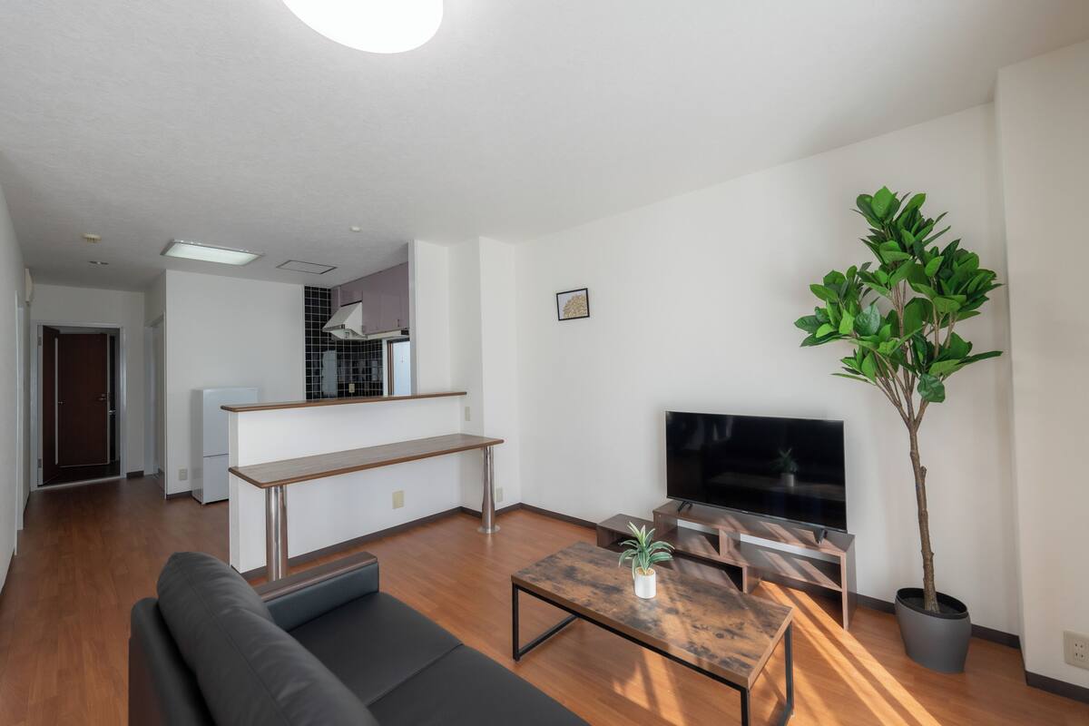 A modern living room with a sofa, coffee table, TV, and a potted plant.