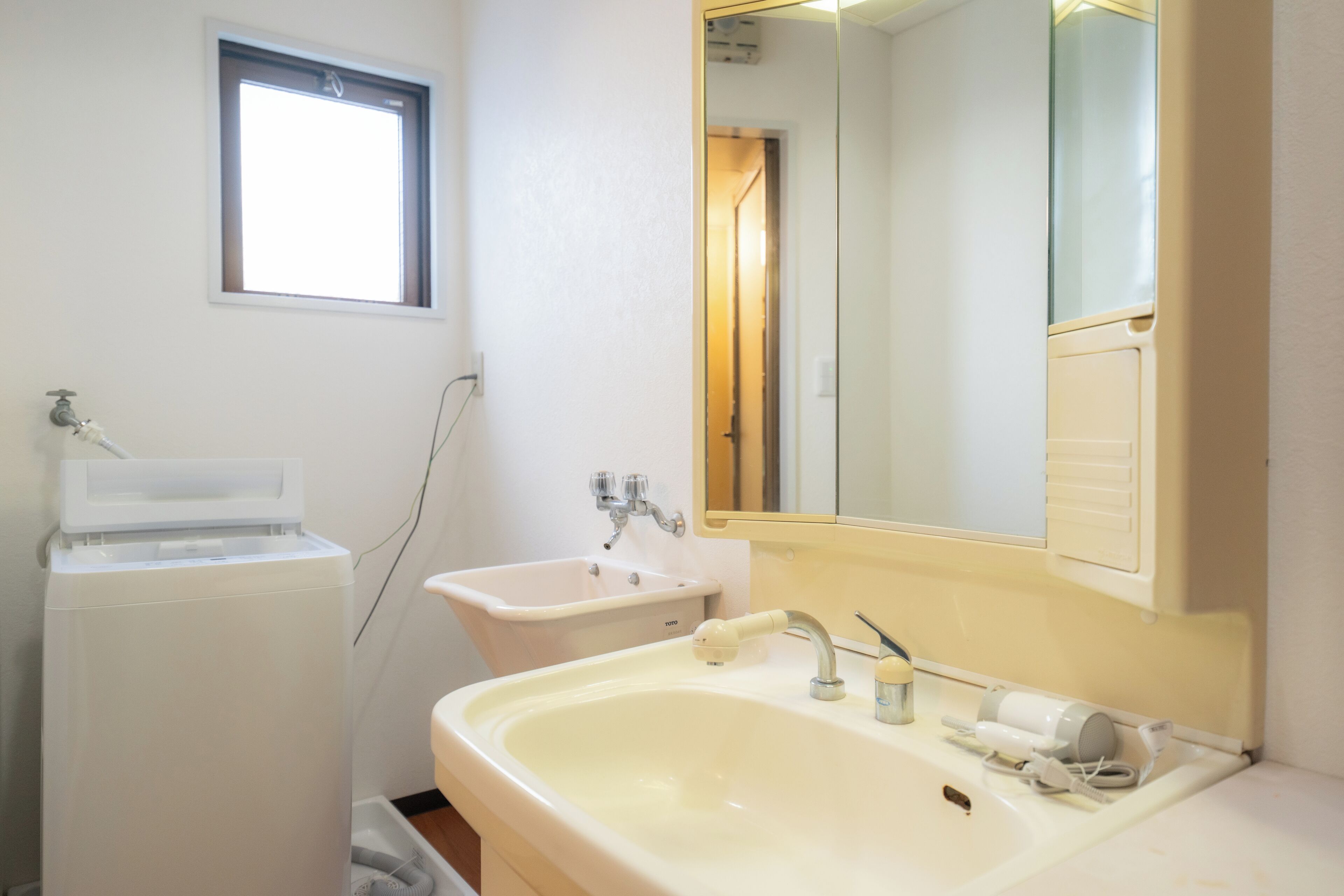 Un baño con un lavabo blanco, un espejo, una ventana y una lavadora blanca.