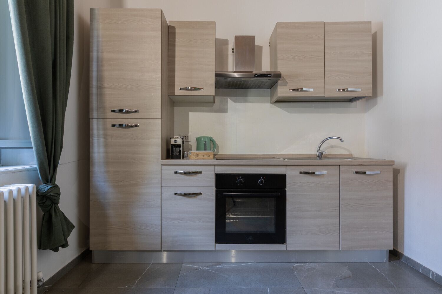 A modern kitchen with light wood cabinetry, a built-in oven, and a stainless steel range hood.