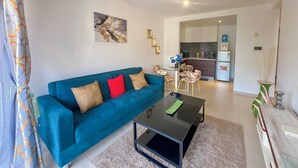 A modern living room with a blue sofa, a glass coffee table, and a kitchen in the background. - Astoria Apartment  (Nairobi)