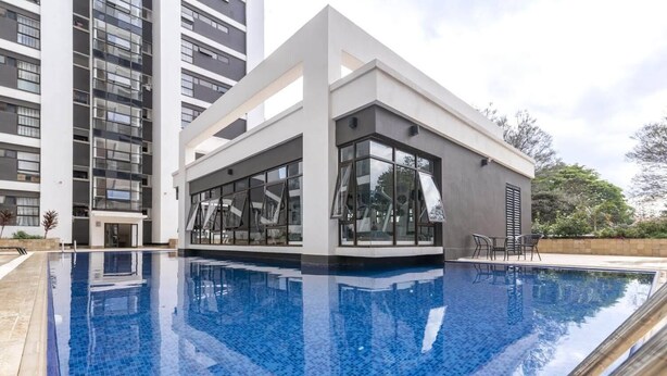 A modern building with a swimming pool, large windows, and a patio area. - Astoria Apartment  (Nairobi)