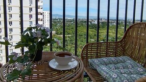 A balcony with a wicker table, a wicker chair, a potted plant, and a cup of coffee. - Studio w Pool, Mountain & City View Mactan Airport (Lapu-Lapu)