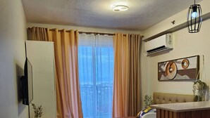 A modern hotel room with a bed, a sofa, a small desk, and a window with curtains. - Studio w Pool, Mountain & City View Mactan Airport (Lapu-Lapu)
