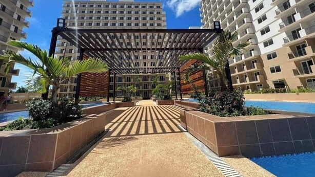 A modern hotel with a pool area, a covered walkway, and high-rise buildings in the background. - Studio w Pool, Mountain & City View Mactan Airport (Lapu-Lapu)