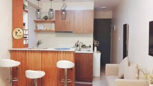 A compact kitchen with wooden cabinets, a built-in bar area with stools, a sink, and a dining area with a sofa. - Studio w Pool, Mountain & City View Mactan Airport (Lapu-Lapu)