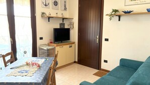 A compact living space with a dining table set for two, a sofa, a television, and decorative wall art. - Apartment With Pool View-beahost (San Michele al Tagliamento)