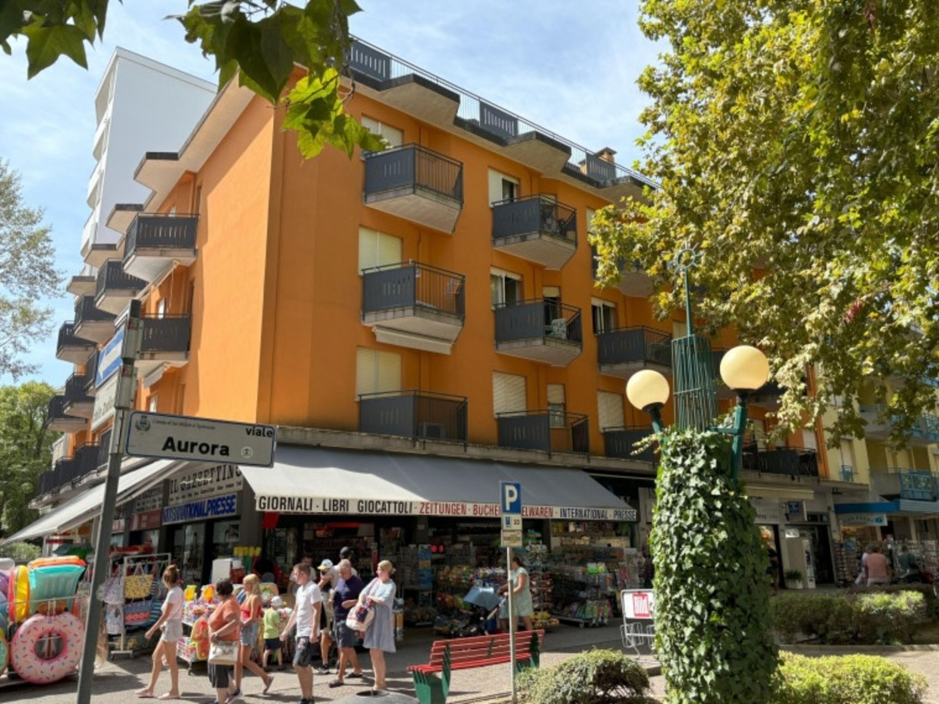 A multi-story building with balconies, a storefront with various signs, and people walking on the sidewalk.