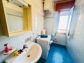 A bathroom with a white sink, a mirror, a toilet, and a shower area. - Colorful Flat in Bibione-beahost (San Michele al Tagliamento)