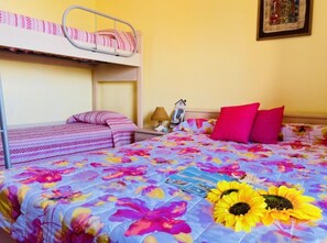 A dormitory room with bunk beds, a bed with a floral bedspread, and a framed picture on the wall. - Colorful Flat in Bibione-beahost (San Michele al Tagliamento)