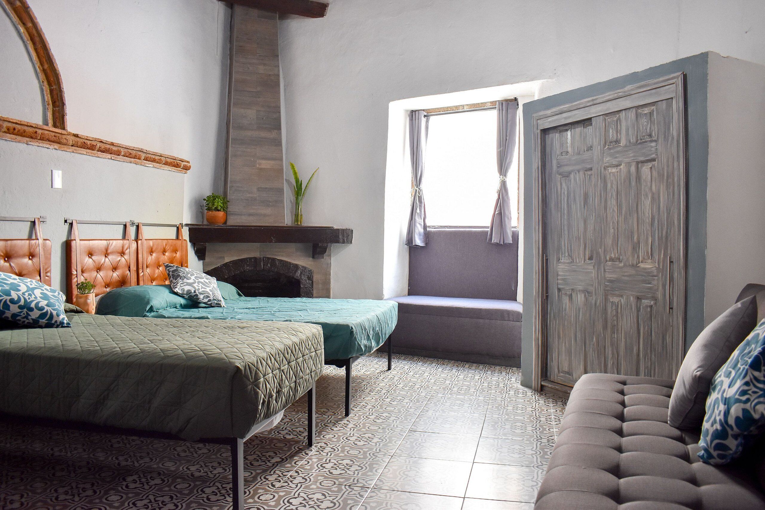 A bedroom with two beds, a sofa, a fireplace, and a window with curtains.