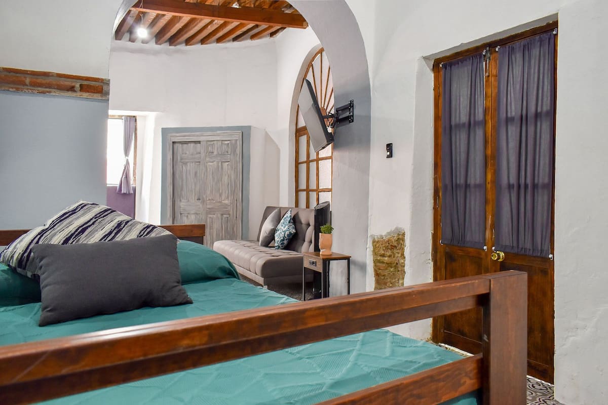 A bedroom with a bed, a wooden headboard, a nightstand, a dresser, a window with curtains, and a door.