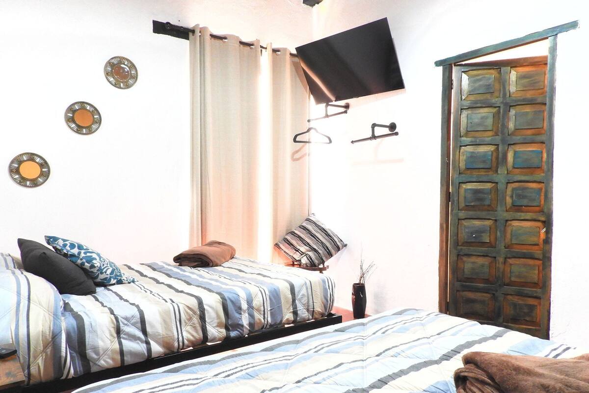 A bedroom with a bed, a TV mounted on the wall, a door, and a window with curtains.