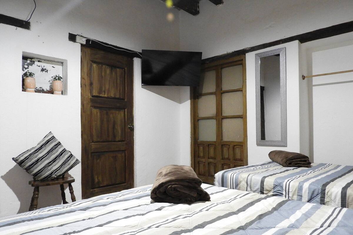 A room with two beds, a wooden door, a mirror, and a small table with a pillow.