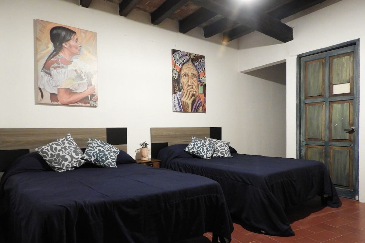 A room with two beds, a wooden door, and two paintings on the wall.