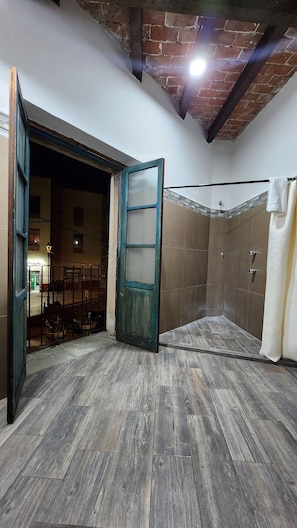 A room with a wooden floor, a door, a shower area, and a visible outdoor area with a street and buildings. - Doña Vicenta Casa Colonial (Guanajuato)
