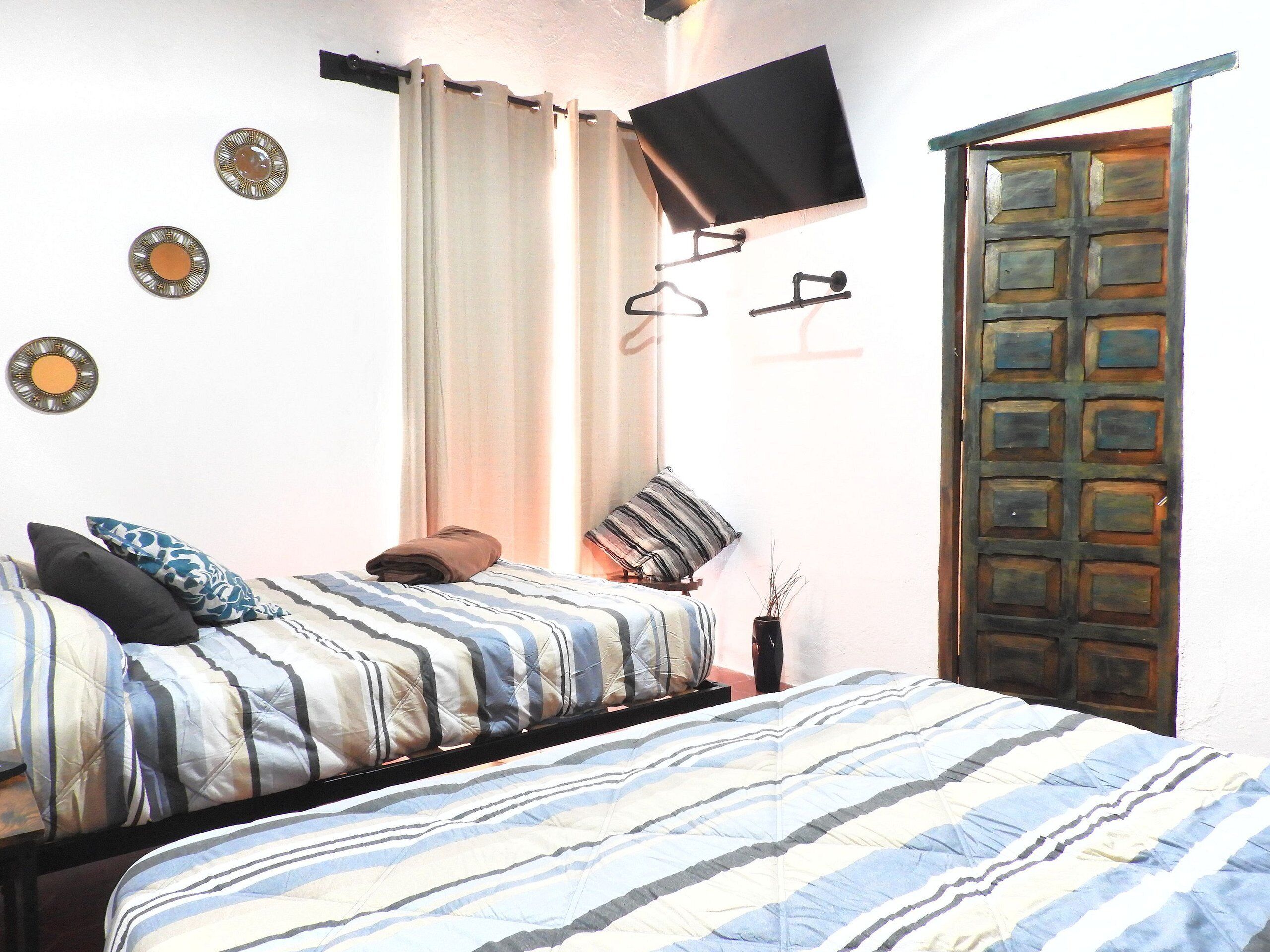 A bedroom with a bed, a TV mounted on the wall, a door, and a curtain.