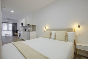 A modern hotel room with a large bed, a bedside table, a built-in washing machine, and a kitchenette. - Dobo Madrid Numancia (Madrid)