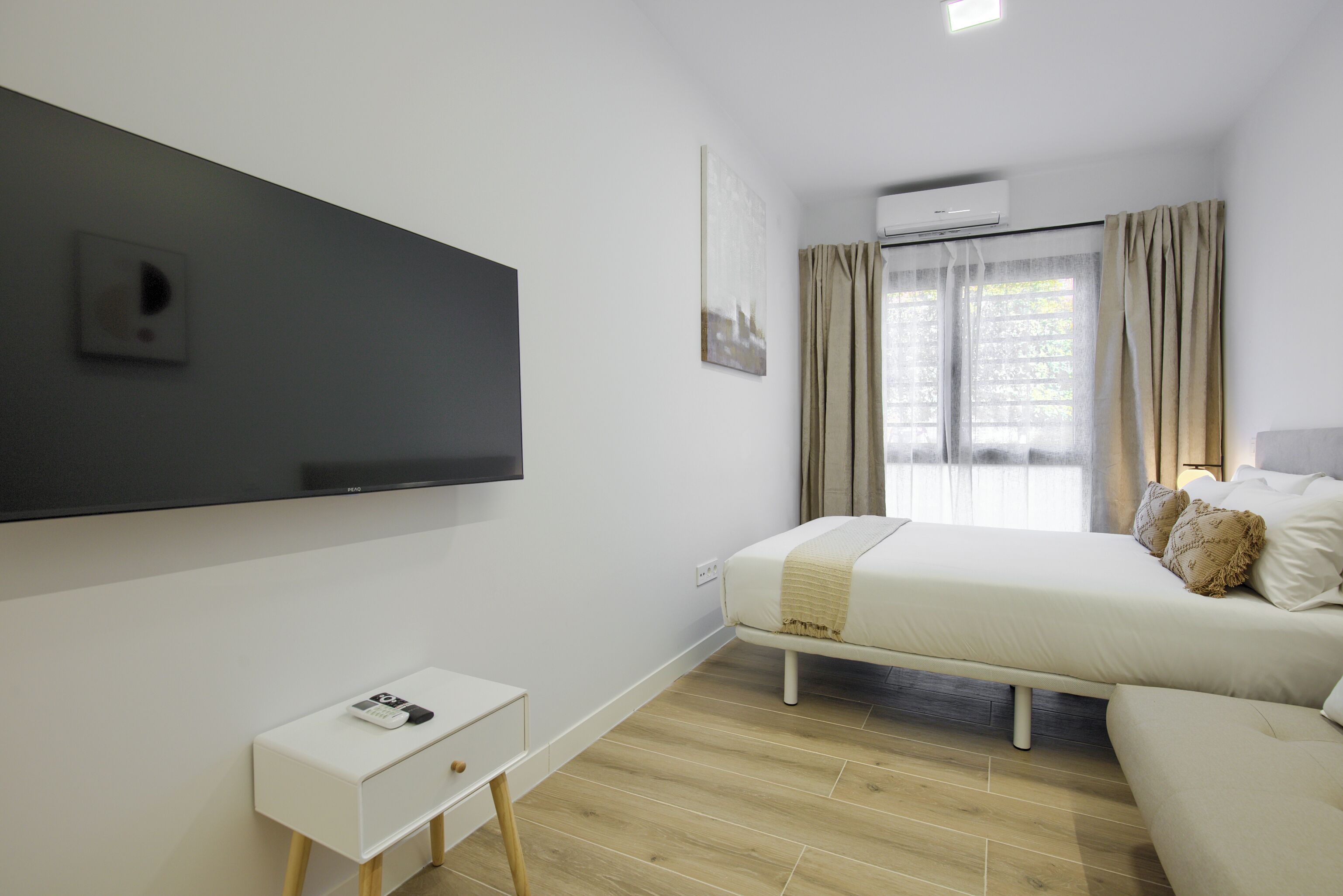 Un dormitorio moderno con cama, mesita de noche y televisor montado.
