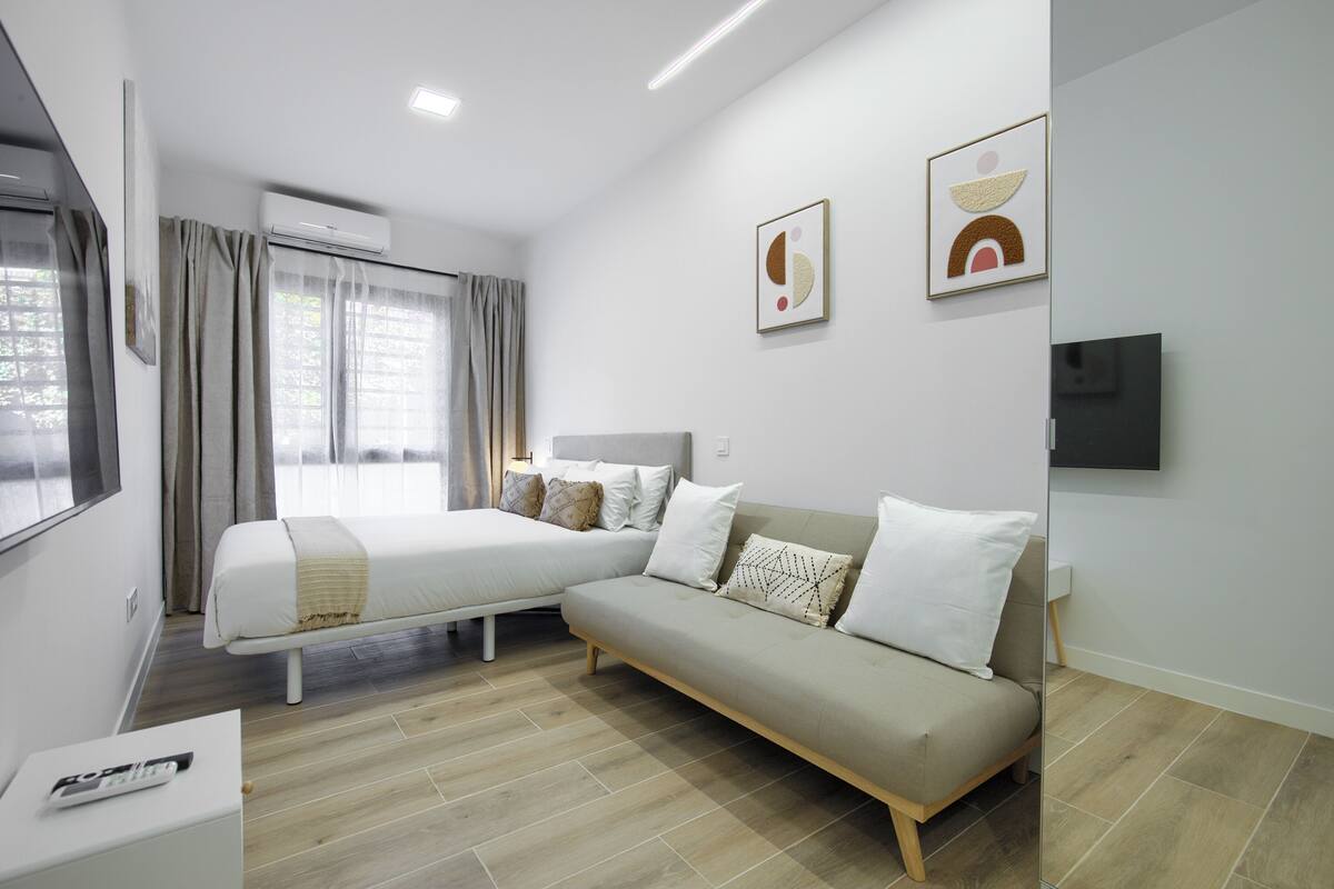 A modern hotel room with a bed, a sofa, a flat-screen TV, and artwork on the walls.