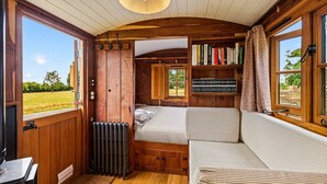 Una habitación acogedora y funcional con cama, un pequeño rincón de descanso, una estantería y una ventana que ofrece vistas al exterior.