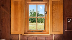 Ventana con marco de madera que da a un área verde y árboles.
