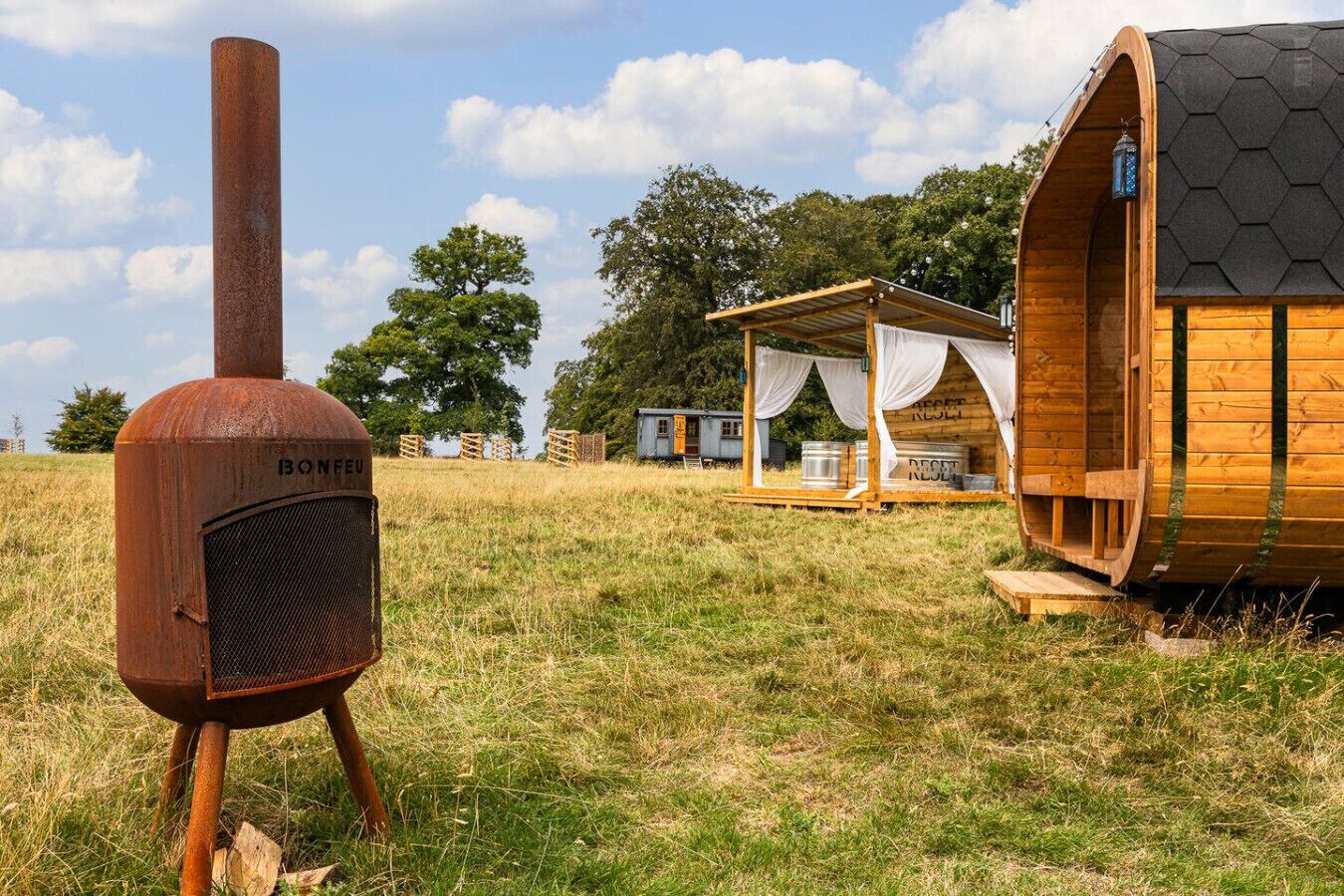 Un entorno rústico al aire libre con una estructura metálica que dice “BONFEEU” y cabañas de madera con techo hexagonal.