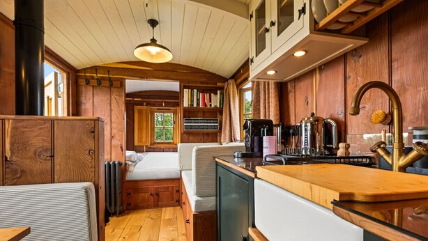 Un interior compacto con paneles de madera, una kitchenette, una cama y una zona de estar.