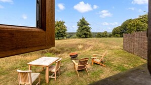 Un espacio al aire libre con mesa y sillas, una parrilla y vistas a un campo cubierto de césped y árboles.