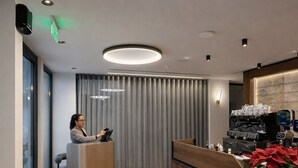 A modern reception area with a wooden reception desk, a digital screen, and a potted plant.