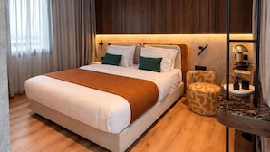 A modern bedroom with a large bed, wooden flooring, a nightstand, and a bedside table with a lamp.
