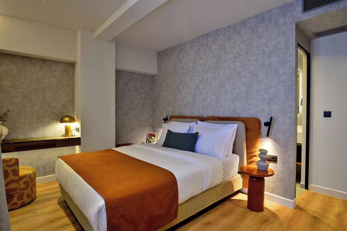 A neatly made bed with a brown blanket, a bedside table with a lamp, and a wall-mounted light.