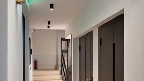 A modern hallway with a staircase, dark doors, and recessed lighting.