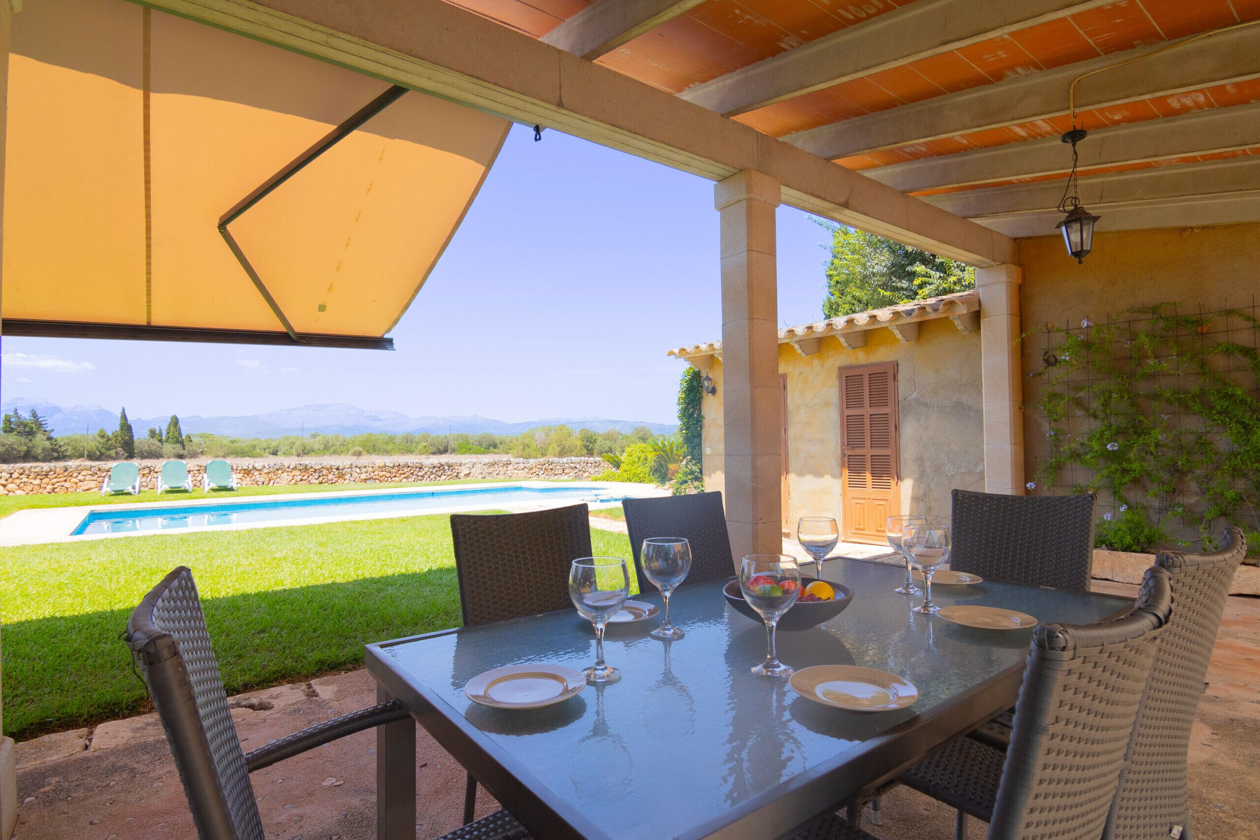 Un patio exterior con una mesa lista para comer, con vistas a una piscina y montañas.