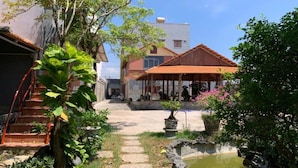 A courtyard with a small pond, a wooden pergola, and a building with a red roof. - ML Homestay (Ho Chi Minh City)