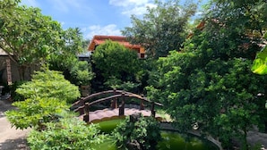 A tranquil garden with a wooden bridge over a pond, surrounded by lush greenery and a traditional house in the background. - ML Homestay (Ho Chi Minh City)
