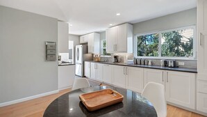 A modern kitchen with white cabinets, a black countertop, and a window providing natural light. - @ Marbella Lane - Chic Abode W/mountain Skyline (Pacifica)
