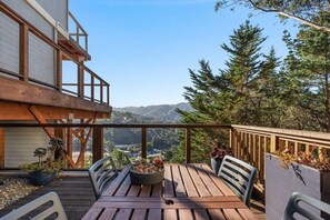 A wooden deck with a table and chairs, surrounded by potted plants and overlooking a mountainous landscape. - @ Marbella Lane - Chic Abode W/mountain Skyline (Pacifica)