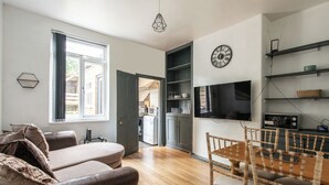 A modern living room with a sofa, dining table, and chairs, a kitchen area with cabinets and appliances, and a large window. - Fentonville House (Sheffield)