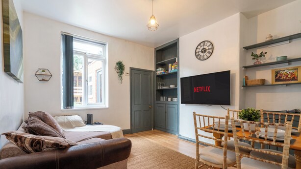 A modern living room with a sofa, a dining table with chairs, a TV mounted on the wall, and a bookshelf. - Fentonville House (Sheffield)