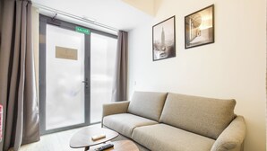 A hotel room with a sofa, a coffee table, a door with a sign, and two framed pictures on the wall. - Dobo Madrid Río (Madrid)