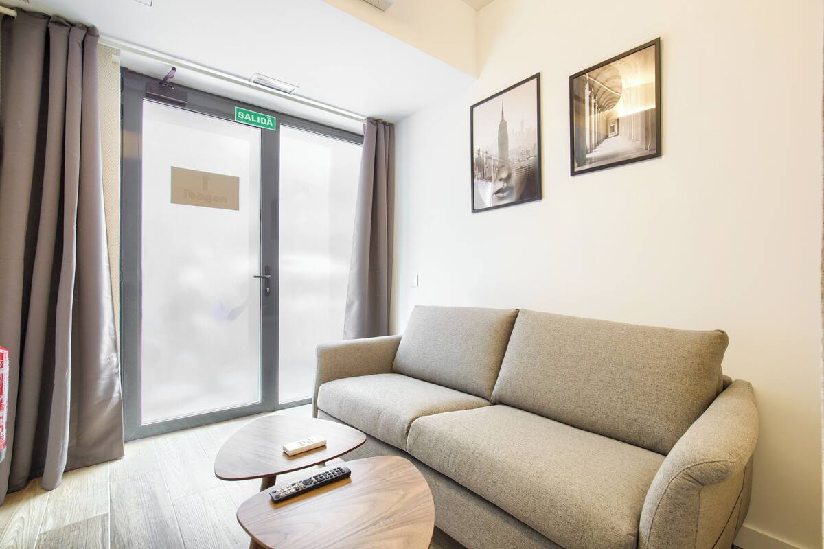 A hotel room with a sofa, a coffee table, a door with a sign, and two framed pictures on the wall.