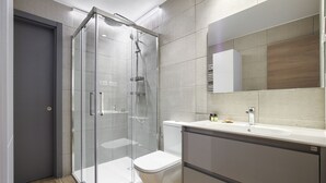 A modern bathroom with a glass-enclosed shower, a toilet, and a vanity with a mirror. - Dobo Madrid Río (Madrid)