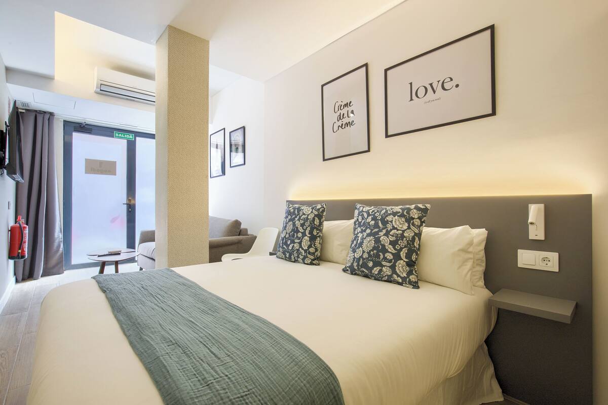 A hotel room with a large bed, two pillows, a bedside table, and a wall-mounted light.