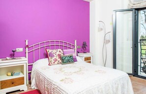 Um quarto com cama, mesas de cabeceira, janela e porta.