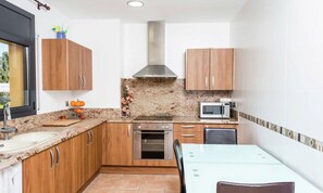 Una cocina compacta con muebles de madera, horno integrado, microondas y un comedor con mesa y sillas.