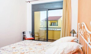 Un dormitorio con cama, una silla, una lámpara y vistas de un edificio a través de puertas correderas.