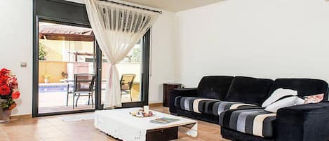 Uma sala de estar com um sofá preto, uma mesa de centro e uma porta de vidro deslizante que dá para uma área externa.