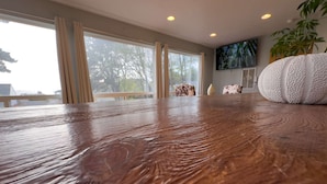 A wooden table in a room with large windows, a mounted TV, and a potted plant. - "Sea Song": Ocean Views, 2BD*, Ping Pong, Foosball (Crescent city)
