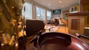 A modern living room with a large wooden coffee table, a sofa, and a dining area with a TV mounted on the wall. - "Sea Song": Ocean Views, 2BD*, Ping Pong, Foosball (Crescent city)